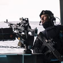 blue uniformed and beret wearing royal Navy Gunner surveying for threats with general purpose machine gun in foreground