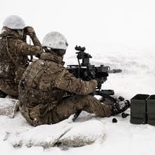 Marine sat in the snow firing a heavy machine gun