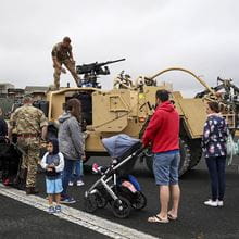 Families stood around looking at an armoured vehicle with a marine stood on top