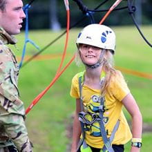 Small girl in a yellow t-shirt in a harness and helmet being assisted by a marine