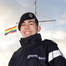 Top-half crop of Navy officer smiling standing in front of a pride flag