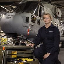 A female AET poses in front of a merlin helicopter