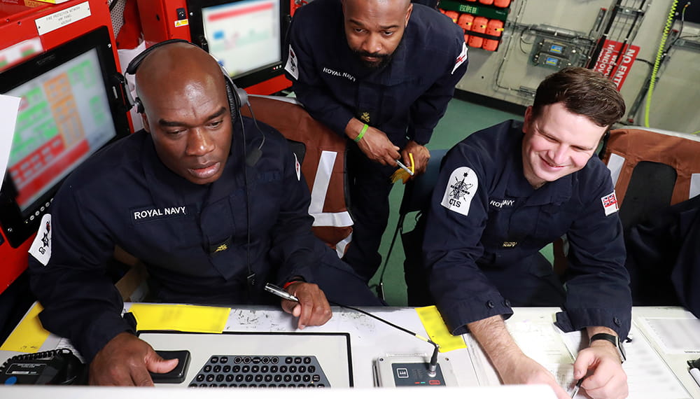 three uniformed royal navy personnel looking at computer screen