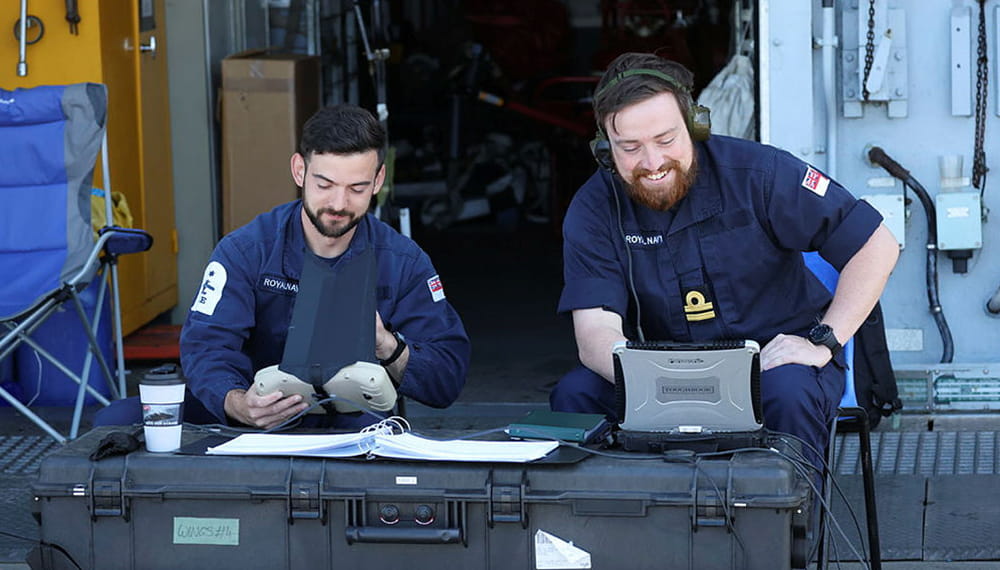 Two navy personnel working and smiling with equipment. 