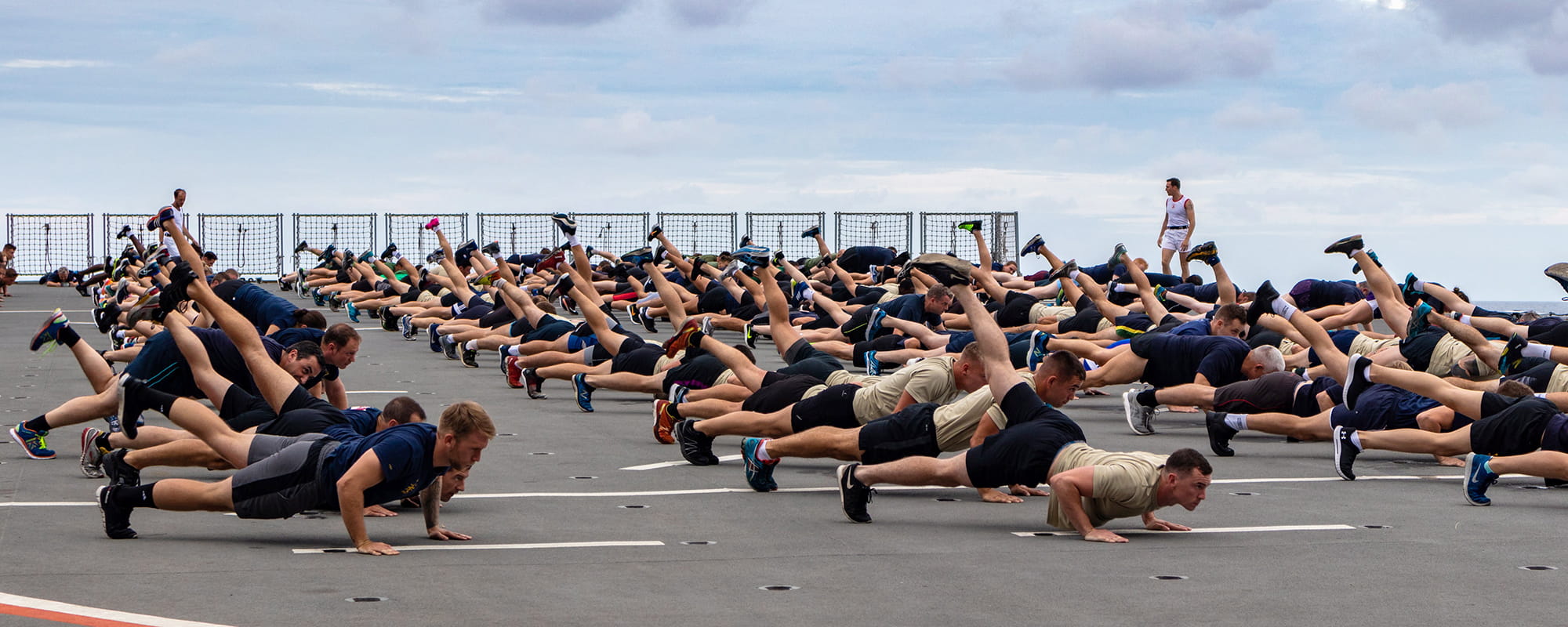 Pictured is PTI (Physical Training Instructor) Cpl Andrew Orchard of 40 Commando, Royal Marines taking the ship’s company and Charlie Company for an IMF (Initial Military Fitness) session on the flight deck of HMS Albion.