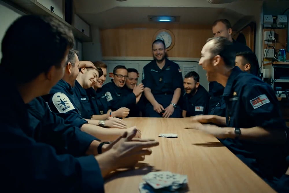 blue uniformed royal navy personnel in on board mess sitting round table laughing and chatting