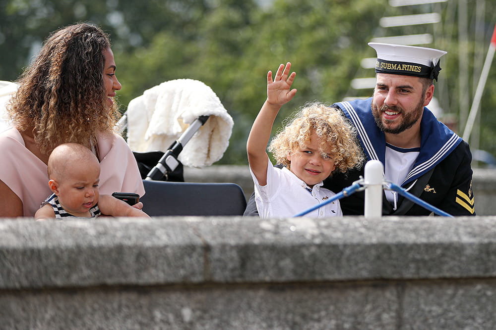 uniformed royal navy rating with family with child waving to camera