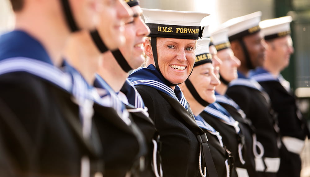 HMS Forward personnel standing in a line at the Royal Navy Reserve unit in Birmingham. One sailor smiles at the camera.