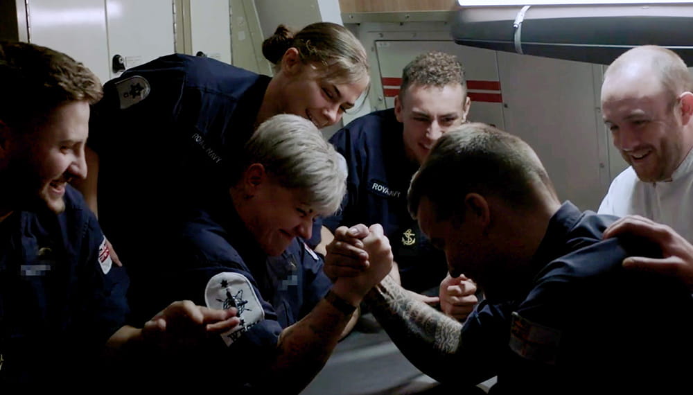 Ship company smiling and watching a playful arm wrestle. The navy is built on trust and support. Living, working and socialising together in a unique under sea environment. 