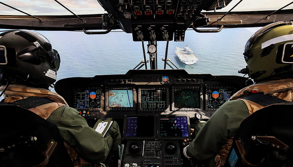 Helicopter crew navigating to land aboard HMS Prince of Wales which is visible in through the windscreen