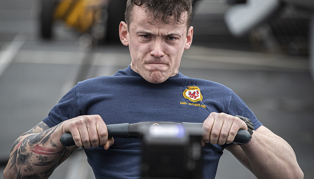 Man pulling on the handles of a rowing machine grimacing