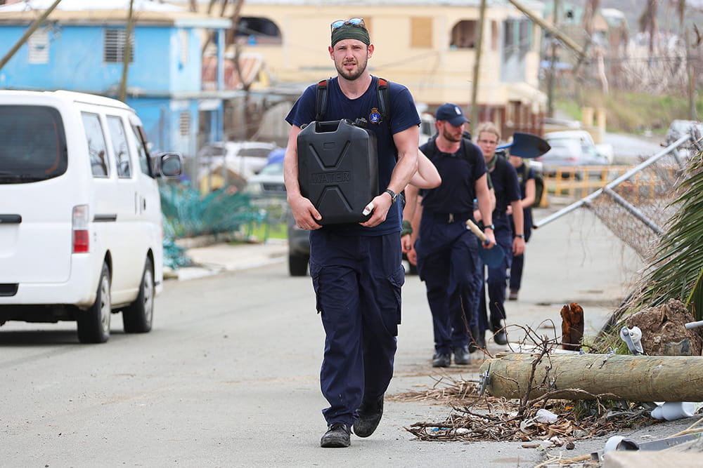 Sailors carry supplies through the aftermath of a hurricane