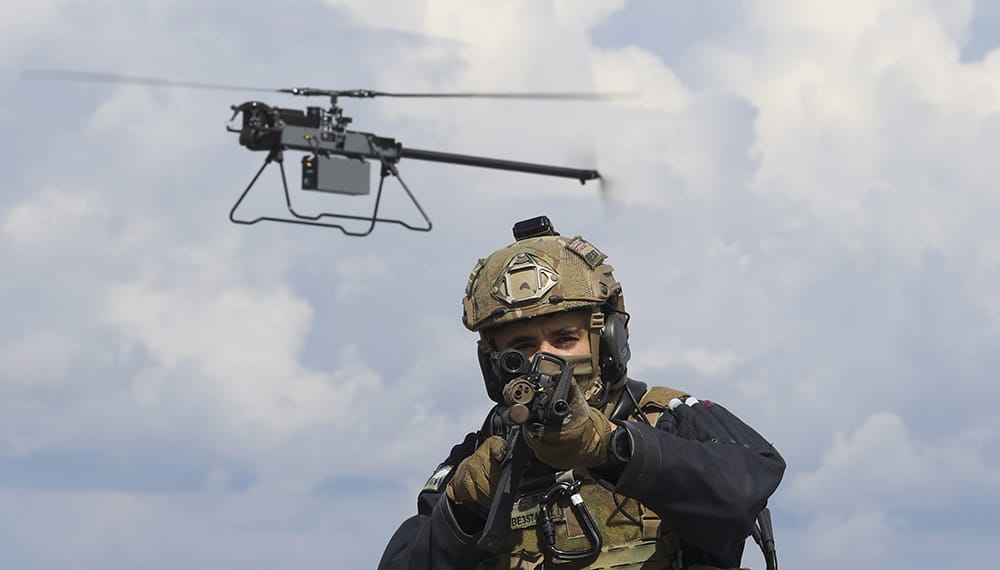 An Anduril Ghost drone hovering over the head of a marine who is aiming a weapon at the camera