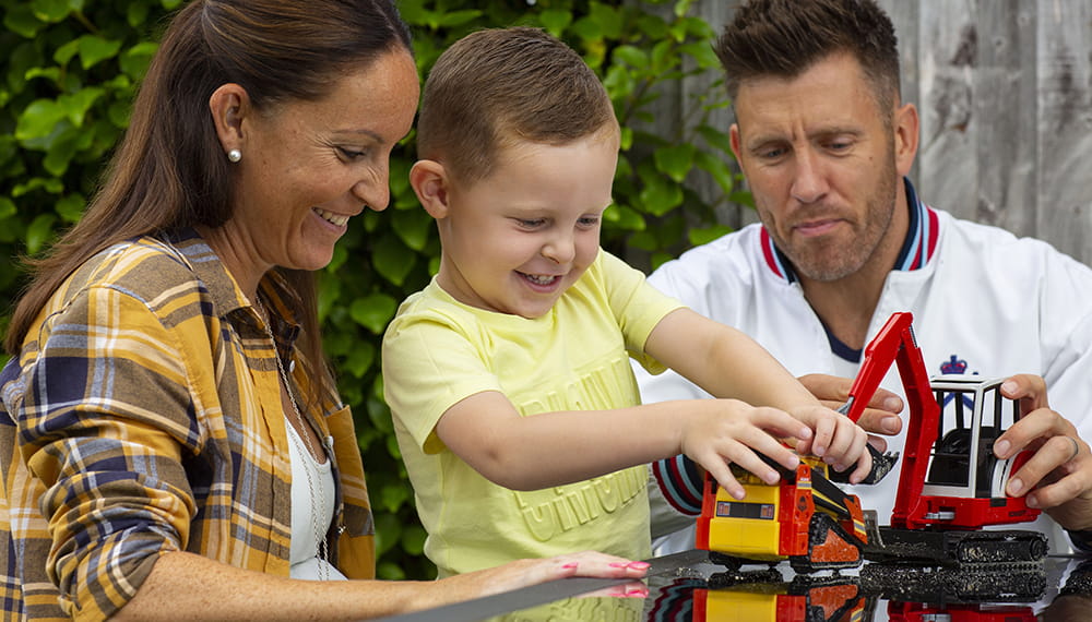 Mother and father with son playing with a toy digger