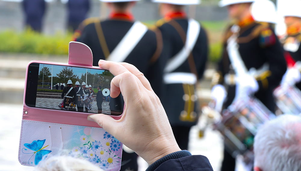 Grey-haired woman holding up a digital camera with marching band displayed the screen