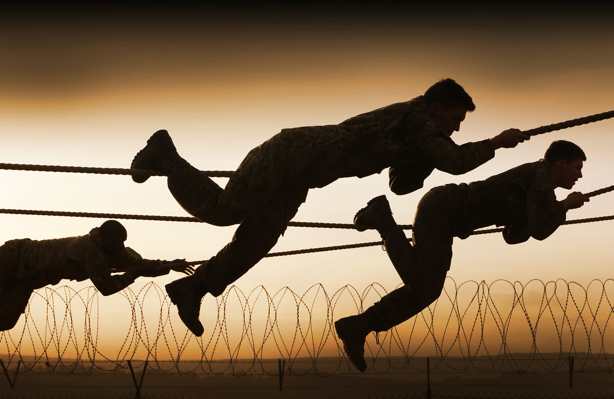 Silhouettes of Royal Navy personnel climbing along ropes above barbed wire