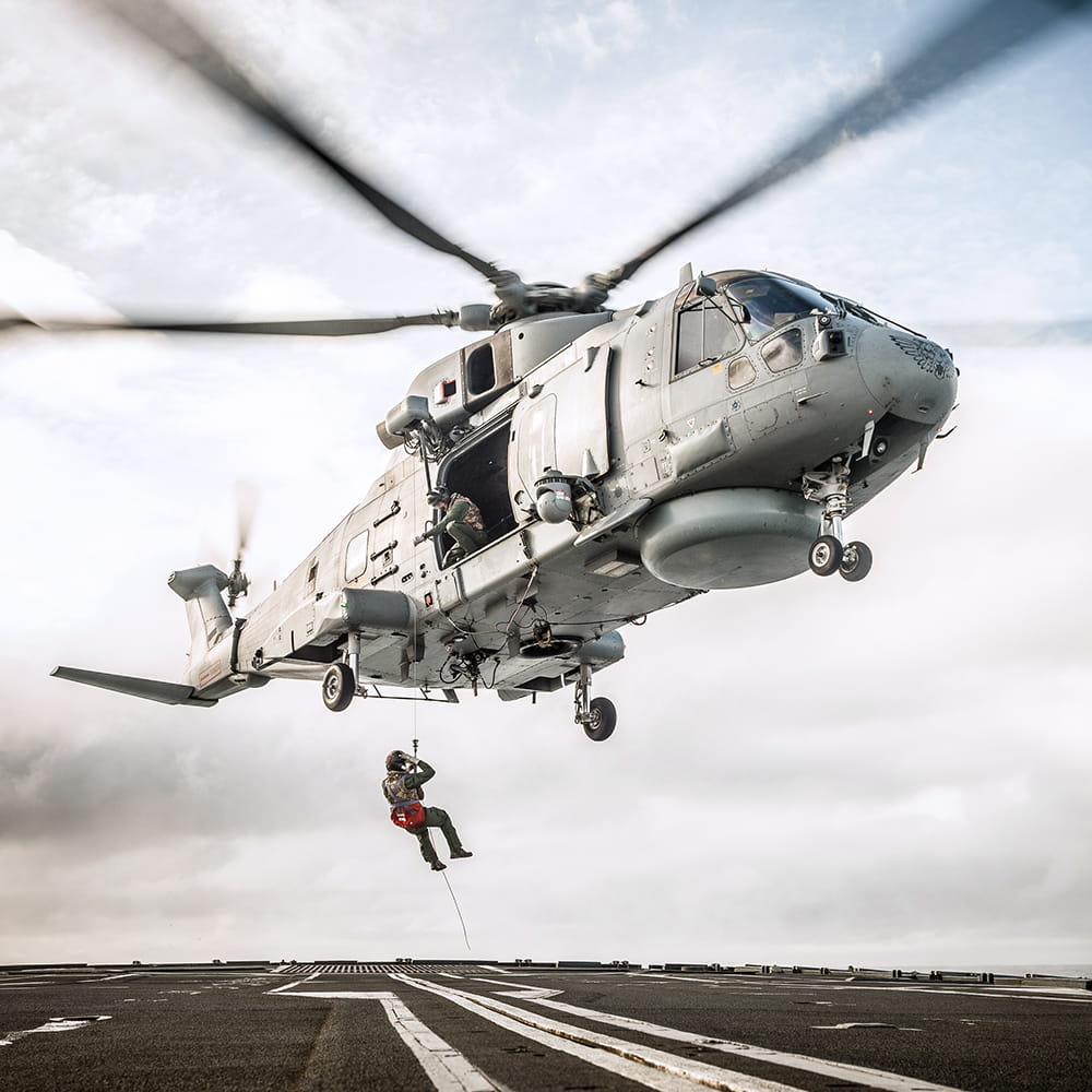 Royal Marine descends from a flying helicopter on a rope onto a ship's deck