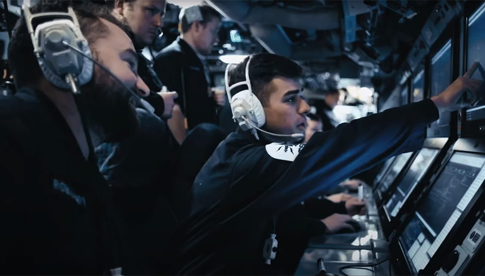 Royal Navy crew members in a control room wearing headphones point at screens