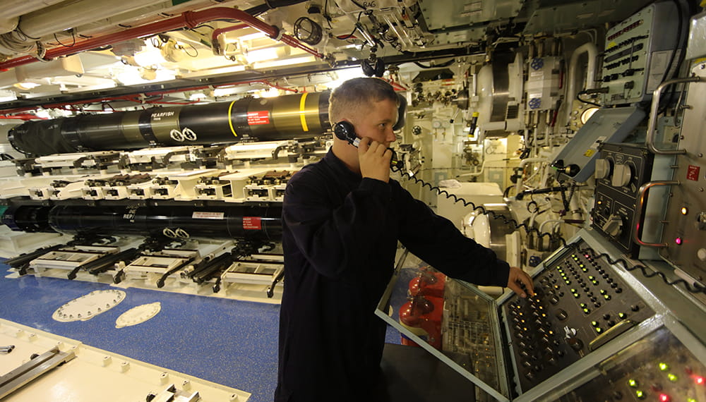 Man on phone in a submarine missile room operating a panel