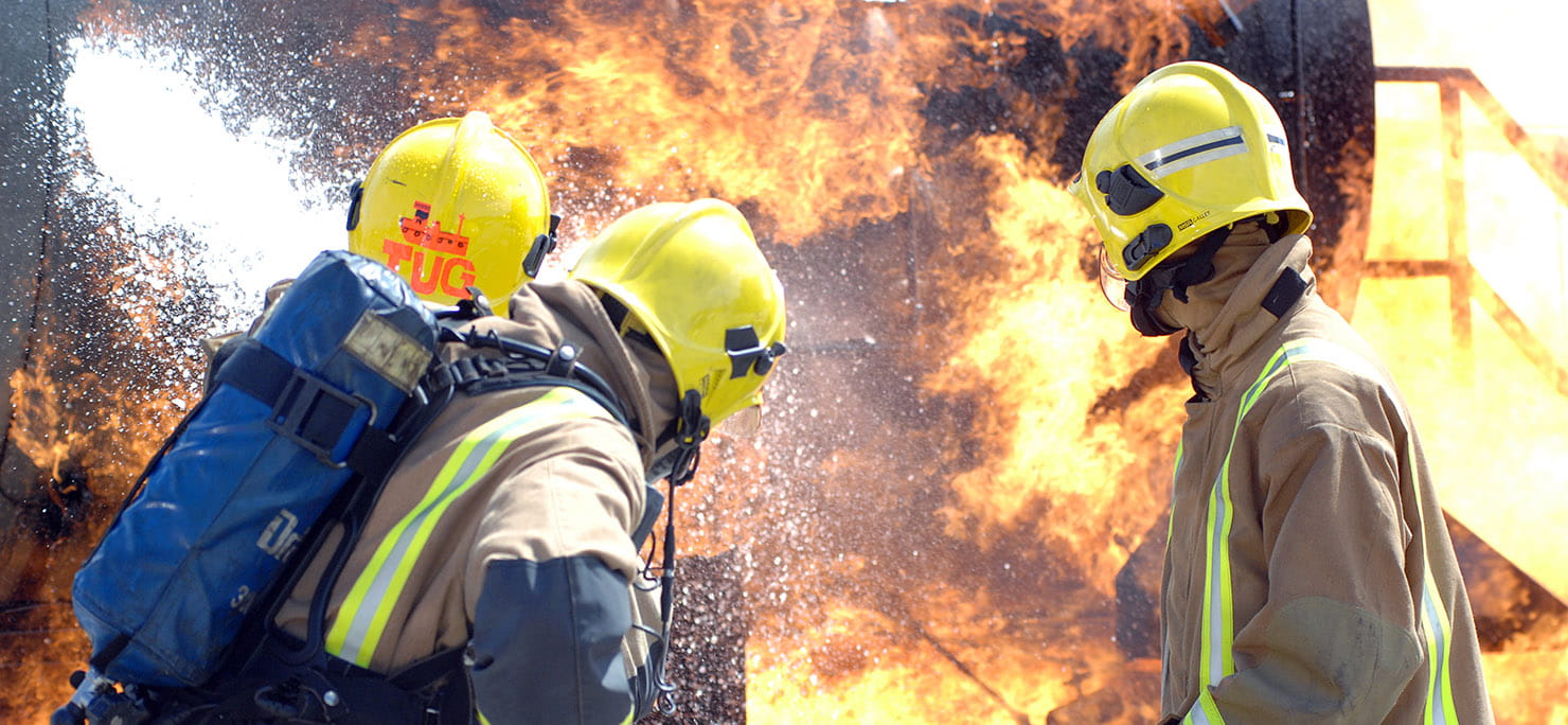 Three personnel attending to a large fire during firefighting exercise.
