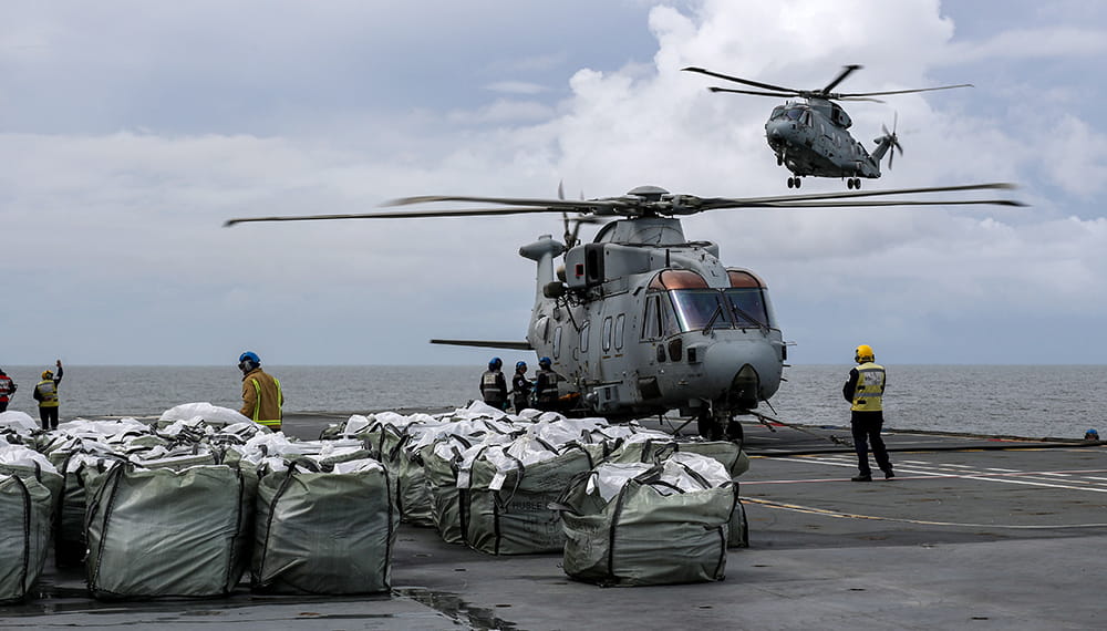 Merlin helicopter aboard the deck of an aircraft carrier surrounded by humanitarian aid supplies